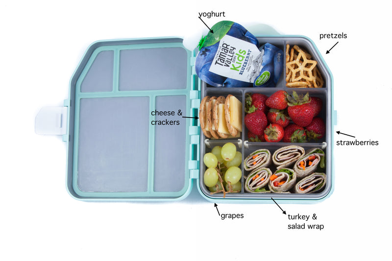 A delicious kids lunchbox includes colourful and healthy food. Here we have turkey & salad wrap cut into sushi pieces which are perfect for little hands and mouths, green grapes, cheese and crackers, yogurt pouch, stawberries and pretzels.